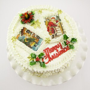 K&ouml;nnte beinhalten: Ein wei&szlig;er Kuchen, verziert mit wei&szlig;em Frosting, rotem Stechpalmenlaub, goldenen Sternen und Vintage-Weihnachtsbildern. Der Kuchen ist mit den Worten "Frohe Weihnachten" beschriftet.