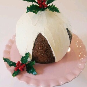 May include: A chocolate cake decorated with white frosting and holly sprigs with red berries. The cake is on a pink cake stand.