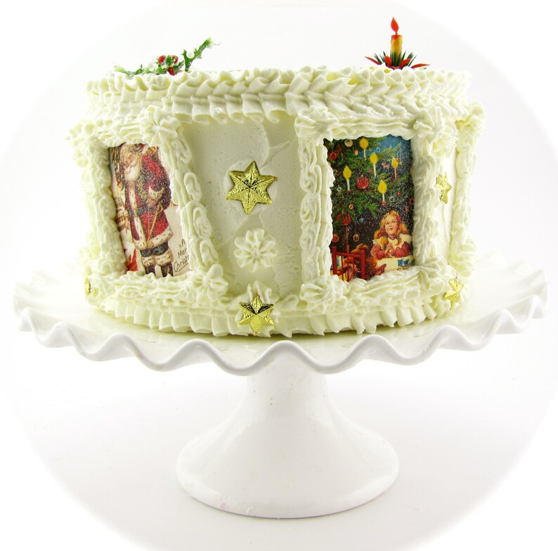 K&ouml;nnte beinhalten: Ein wei&szlig;er Kuchen, der mit wei&szlig;em Frosting und einem gewellten Rand verziert ist. Der Kuchen ist mit Bildern von Weihnachtsszenen und goldenen Sternen verziert. Der Kuchen steht auf einem wei&szlig;en Kuchenst&auml;nder.