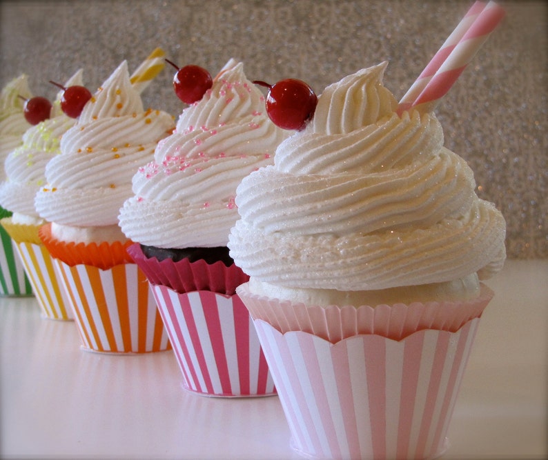May include: Five cupcakes with white frosting and red cherries on top. The cupcakes are in striped paper liners. The liners are pink and white, orange and white, and green and white.