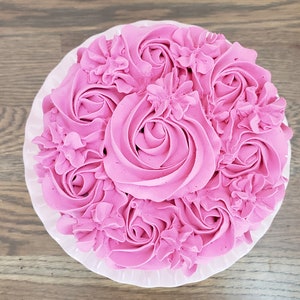 Puede incluir: Un pastel rosa decorado con glaseado rosa en forma de rosas y flores.