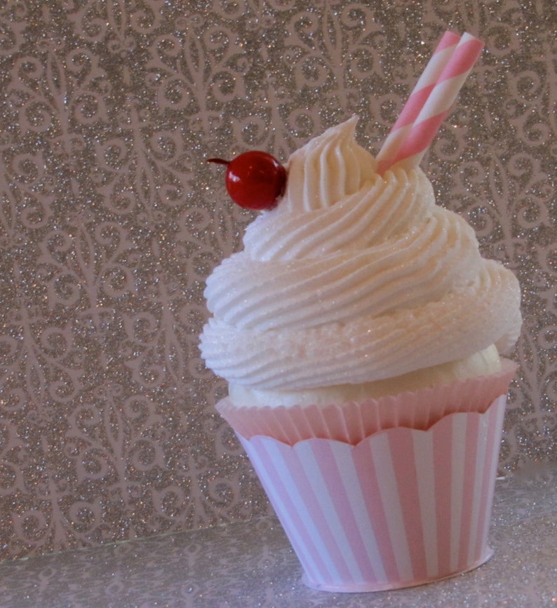 May include: A pink and white striped cupcake with white frosting and a red cherry on top. A pink and white striped straw is sticking out of the frosting.