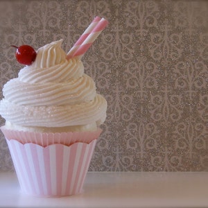May include: A pink and white striped cupcake with white frosting and a red cherry on top. A red and white striped straw is sticking out of the frosting.