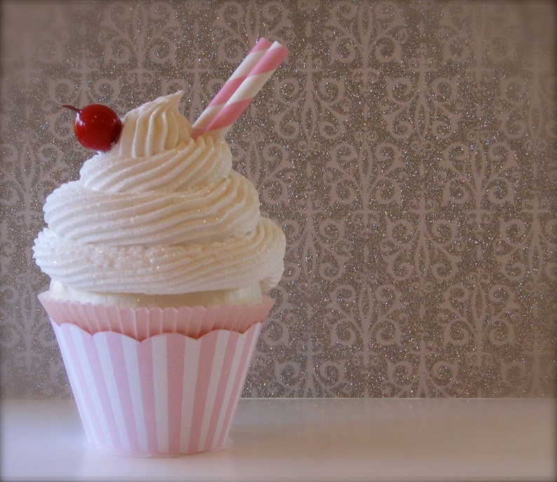 May include: A pink and white striped cupcake with white frosting and a red cherry on top. A red and white striped straw is sticking out of the frosting.