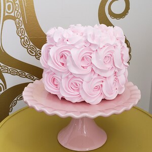 Puede incluir: Un pastel rosa decorado con glaseado rosa en forma de rosas, sobre un soporte para pastel rosa.