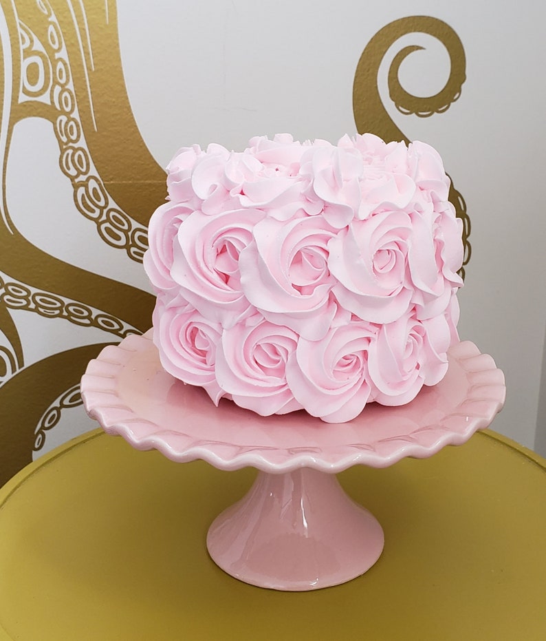 Puede incluir: Un pastel rosa decorado con glaseado rosa en forma de rosas, sobre un soporte para pastel rosa.