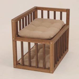May include: A wooden pet bed with two light brown, tufted cushions. The bed has a cage-like structure made of vertical wooden slats and horizontal beams. The wood has a natural finish. The bed is designed for small pets.