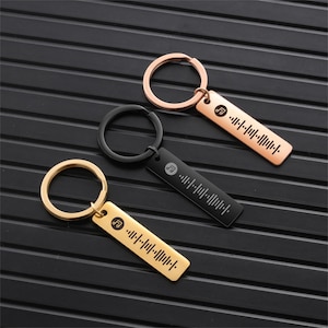 May include: Three keychains with a music note and a barcode design. The keychains are gold, black, and rose gold.