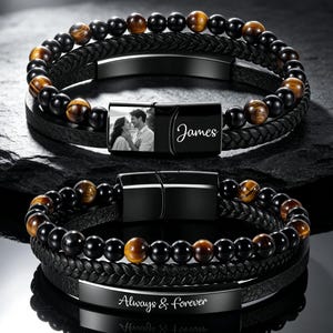 May include: Two multi-strand bracelets featuring black braided leather cords and alternating black and brown tiger eye beads. One bracelet has a black metal clasp with a photo of a couple and the name James. The other has a black metal plate engraved with Always & forever.