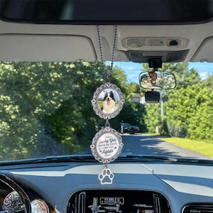 May include: A car charm featuring a black and white dog photo in a decorative frame. Below, a circular charm reads "I will carry you with me until I see you again" with paw prints. A silver paw print charm hangs below.