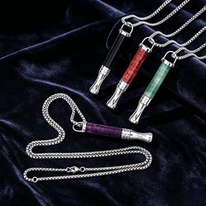 May include: Four necklaces with pendants in various colors: black, red, green, and purple. Each pendant has a silver-colored tip and is suspended from a silver chain. The pendants are cylindrical and appear to be made of different materials.