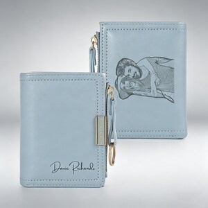 May include: Light blue leather wallet with a gold zipper and key ring. The front of the wallet has the name "Davie Richards" in script. The back of the wallet has a black and white image of a couple. The wallet is approximately 4 inches wide and 3 inches tall.
