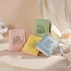 May include: Four small, colorful wallets with engraved portraits. The wallets are in pastel pink, yellow, green, and blue. Each wallet has a zipper closure and a key ring. The portraits appear to be of couples and friends.