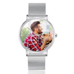May include: Silver wristwatch with a round face featuring a color photo of a person in a red plaid shirt with a dog. The watch has a silver mesh band.