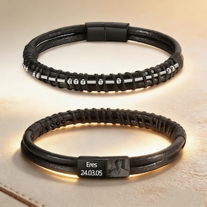 Könnte beinhalten: Zwei schwarze Lederarmbänder. Eines hat silberne Perlen und einen schwarzen Verschluss. Das andere hat einen schwarzen Verschluss mit dem Wort "Eres", dem Datum "24.03.05" und einem kleinen Foto.
