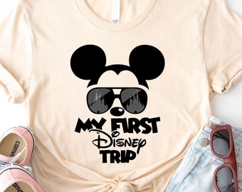 May include: A beige t-shirt with a black Mickey Mouse wearing sunglasses and the text "My First Disney Trip".