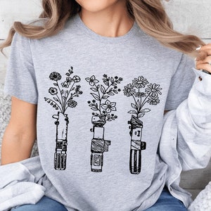 May include: A gray t-shirt with a black and white graphic of three lightsabers with flowers growing out of the top.
