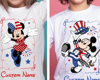 May include: White t-shirts featuring cartoon characters Minnie Mouse and Mickey Mouse in patriotic outfits. Minnie wears a red polka-dot dress and a bow. Mickey holds a hat and cane. The text "Custom Name" is at the bottom.