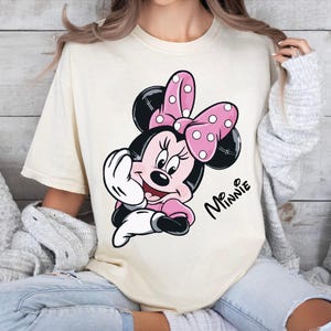 a woman sitting on a bed wearing a mickey mouse t - shirt