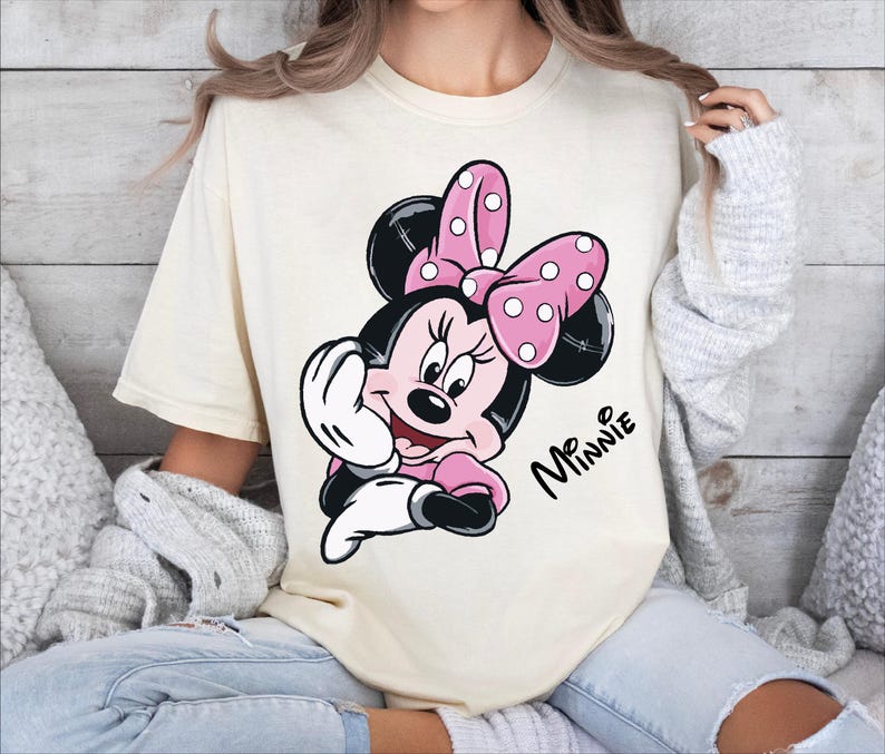 a woman sitting on a bed wearing a mickey mouse t - shirt