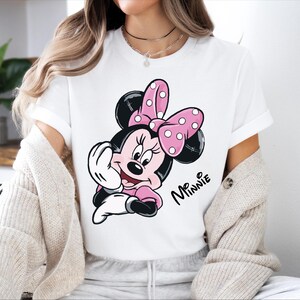 a woman sitting on a bed wearing a minnie mouse t - shirt