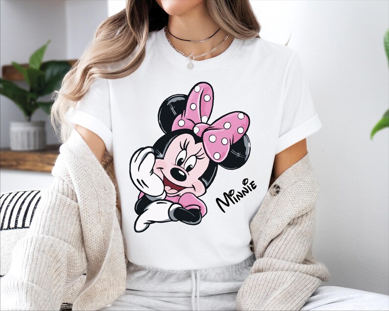 a woman sitting on a bed wearing a minnie mouse t - shirt