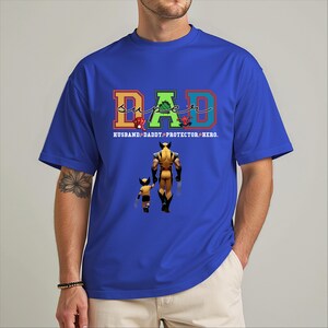 A man wearing a blue t-shirt with a graphic design featuring a superhero character and the text "DAD" in a colorful font.
