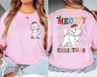 May include: Pink t-shirt with a cartoon cat wearing a Santa hat and Christmas lights. The back of the shirt has the text "MEOWY CHRISTMAS" in colorful letters.