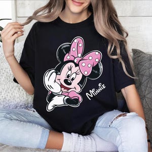 a woman sitting on a couch wearing a minnie mouse t - shirt