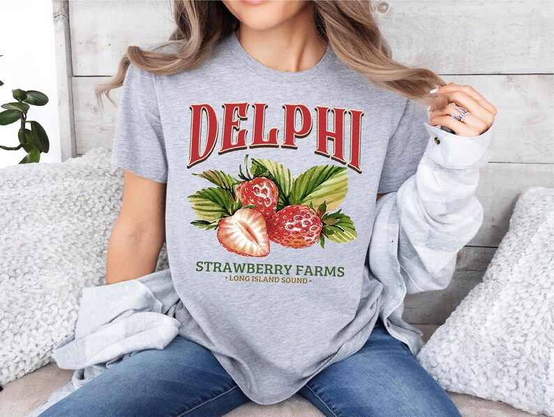 a woman sitting on a bed wearing a delphi strawberry farms shirt