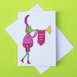 May include: A humorous greeting card showing a green frog in a pink outfit playing a golden trumpet. The trumpet has a red banner with the words "Toots for You". The card is on a white envelope, set against a bright green background.