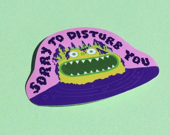 Può includere: Un adesivo fustellato raffigurante un mostro giallo con un'ampia bocca dentata che emerge da una pozza viola scuro. Lo sfondo è rosa chiaro con il testo SORRY TO DISTURB YOU scritto in un carattere viola scuro, irregolare e disegnato a mano.