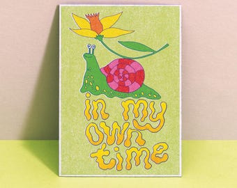 Può includere: Una stampa artistica rettangolare su sfondo verde chiaro raffigurante una lumaca verde con un guscio a motivi rosa e rossi. Sopra la lumaca c'è un fiore giallo con uno stelo verde. Il testo "in my own time" è scritto in lettere gialle.