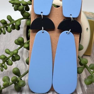 May include: Dangle earrings featuring a light blue square top piece, a black semi-circle middle section, and a long light blue teardrop-shaped bottom piece. The components are connected by silver-toned metal jump rings in a vertical arrangement.