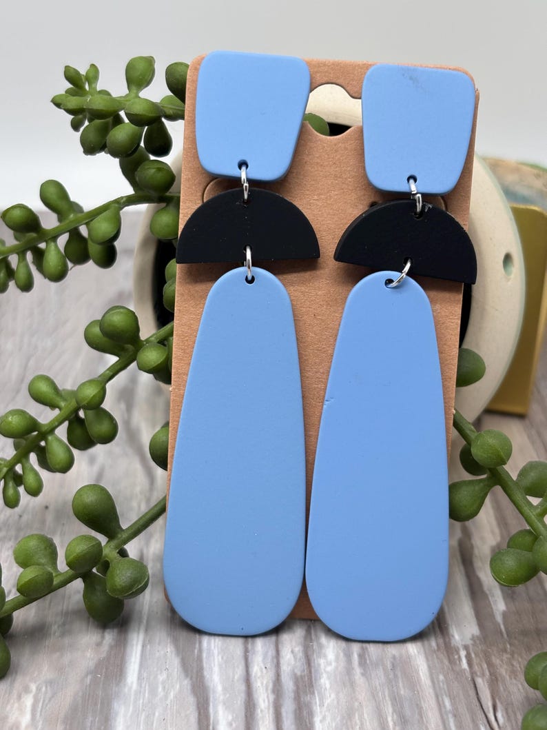 May include: Dangle earrings featuring a light blue square top piece, a black semi-circle middle section, and a long light blue teardrop-shaped bottom piece. The components are connected by silver-toned metal jump rings in a vertical arrangement.