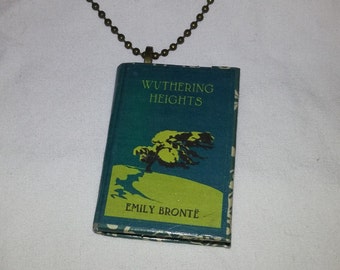May include: A necklace with a miniature book pendant featuring the title "Wuthering Heights" by Emily Brontë. The book cover is teal blue with a green and black illustration of a tree.