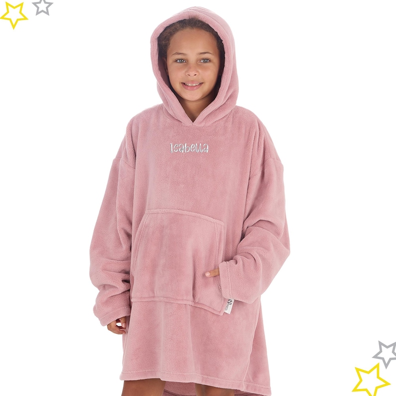 May include: A dusty rose oversized hoodie with a large front pocket and hood. The name "Isabella" is embroidered in silver thread on the chest. The soft, plush material is designed for comfort and warmth. The hoodie is worn by a person.