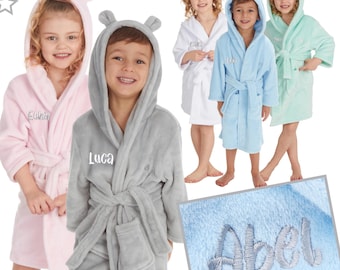 May include: Four children's hooded robes in pink, gray, light blue, and green. The robes have a pocket on the front and a belt. Each robe has a name embroidered on the front:  'Elina', 'Luca', 'Leo', and 'Abel'.