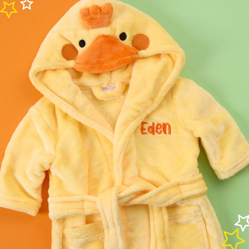 Puede incluir: Batista amarilla con capucha con un dise&ntilde;o de pato en la capucha. La bata tiene un cintur&oacute;n de atar y un bolsillo. La bata est&aacute; personalizada con el nombre "Eden".