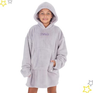 May include: A light gray oversized hoodie with a large front pocket and attached hood. The name "Sophia" is embroidered in purple on the chest. The hoodie is made of a soft, plush material and is designed to be worn as a comfortable garment.