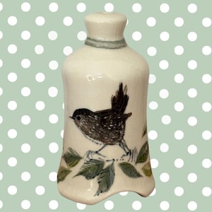 May include: A white ceramic bottle with a bird illustration. The bottle has a narrow neck and a wider base. A small bird with brown and black feathers is perched on a branch with green leaves. A gray band encircles the neck.
