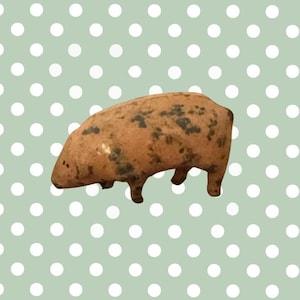May include: A small, brown pig figurine with dark spots. The pig has four short legs and a rounded body. The background is a light green color with white polka dots. This figurine is a decorative item.
