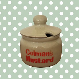 Pode incluir: Um pote de mostarda de cerâmica bege com tampa e uma pequena pega. As palavras "Colman's Mustard" estão impressas em vermelho na frente. A tampa tem uma pequena abertura para uma colher. O fundo é verde claro com bolinhas brancas.