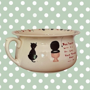Op de afbeelding: Crèmekleurige keramische po met een handvat, met een zwart katten silhouet en een toilet illustratie. Tekst: "Pull Together With An... Your Trouble Away."