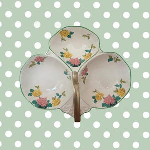 Peut inclure: Plat de service en céramique blanche à trois compartiments, avec une poignée dorée et un bord vert. Il est orné de motifs floraux jaunes et roses. Le fond est vert clair avec des pois blancs.