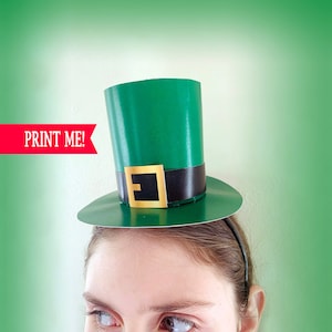 May include: A green paper leprechaun hat with a black band and a gold buckle. The hat is on a person's head.  "PRINT ME!" is written in red on a white background.