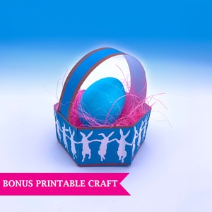May include: A blue and brown paper Easter basket with a pink and white bunny design. The basket is filled with pink shredded paper and a blue Easter egg.