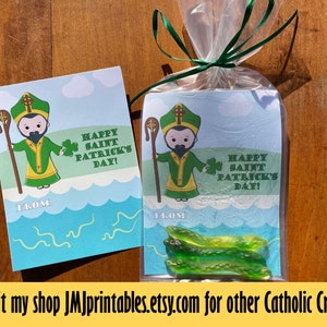 May include: A printable card with a cartoon illustration of Saint Patrick holding a shamrock and a staff. The card says "Happy Saint Patrick's Day!" and has a space to write "From:". The card is next to a clear plastic bag with green gummy worms and a similar card inside.