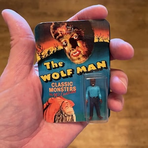Peut inclure: Figurine vintage de l'Homme-Loup, emballée sur une carte bleue et orange. La carte présente le titre du film et un graphisme de monstre classique. La figurine est dans un étui en plastique transparent, avec une chemise bleue et un pantalon noir.