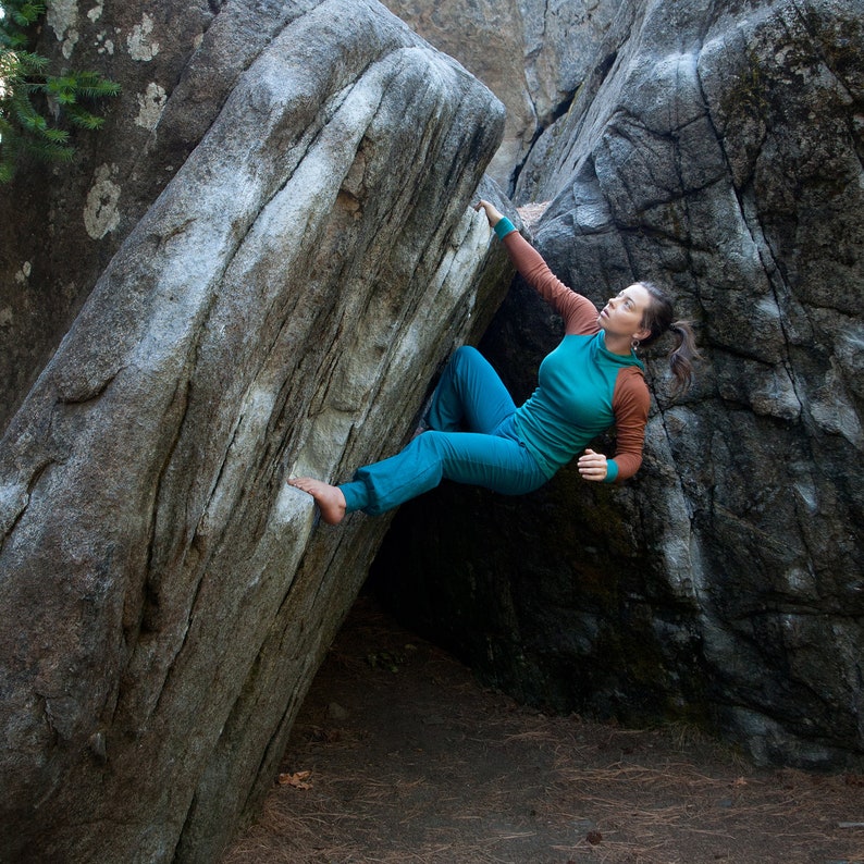 May include: A woman wearing a teal and brown long-sleeved shirt climbs a large, gray rock formation.
